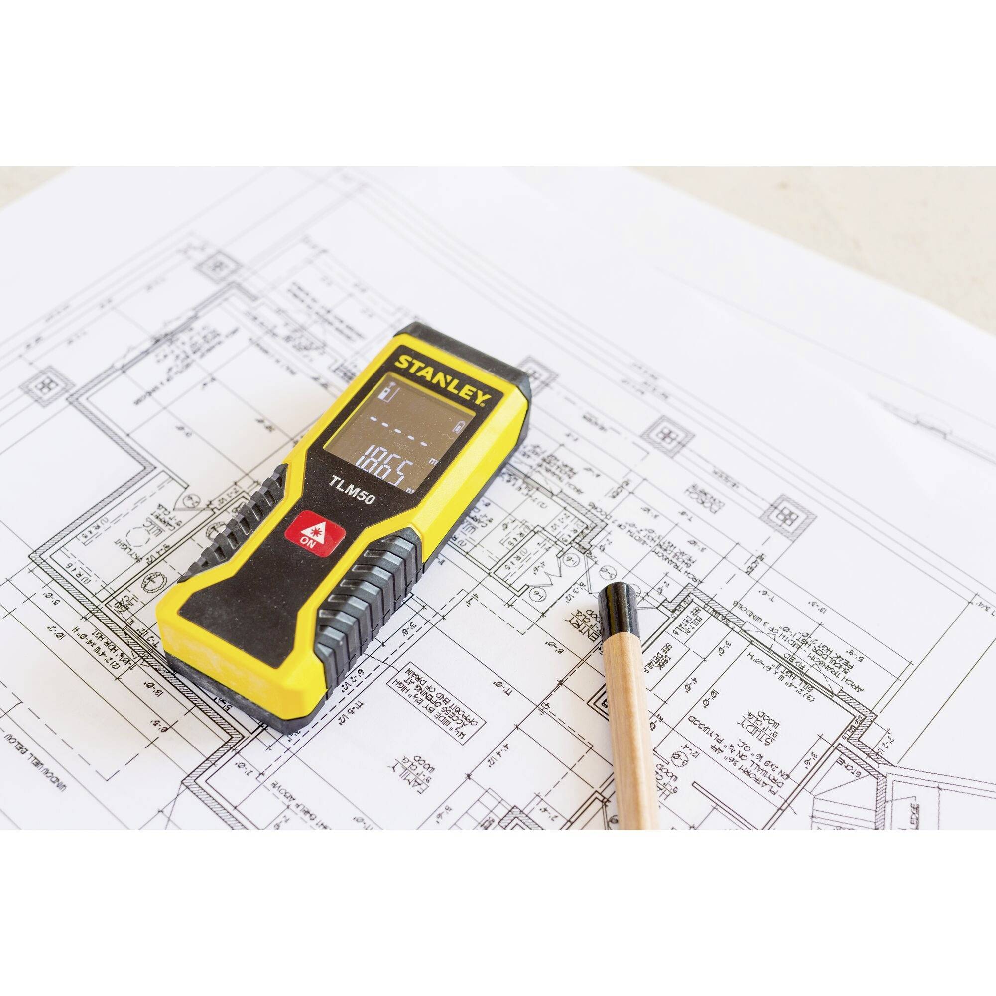 Ein gelbes digitales Messgerät liegt auf einem Bauplan neben einem Bleistift. Das Messgerät zeigt '18.65°C' auf seinem Display an.