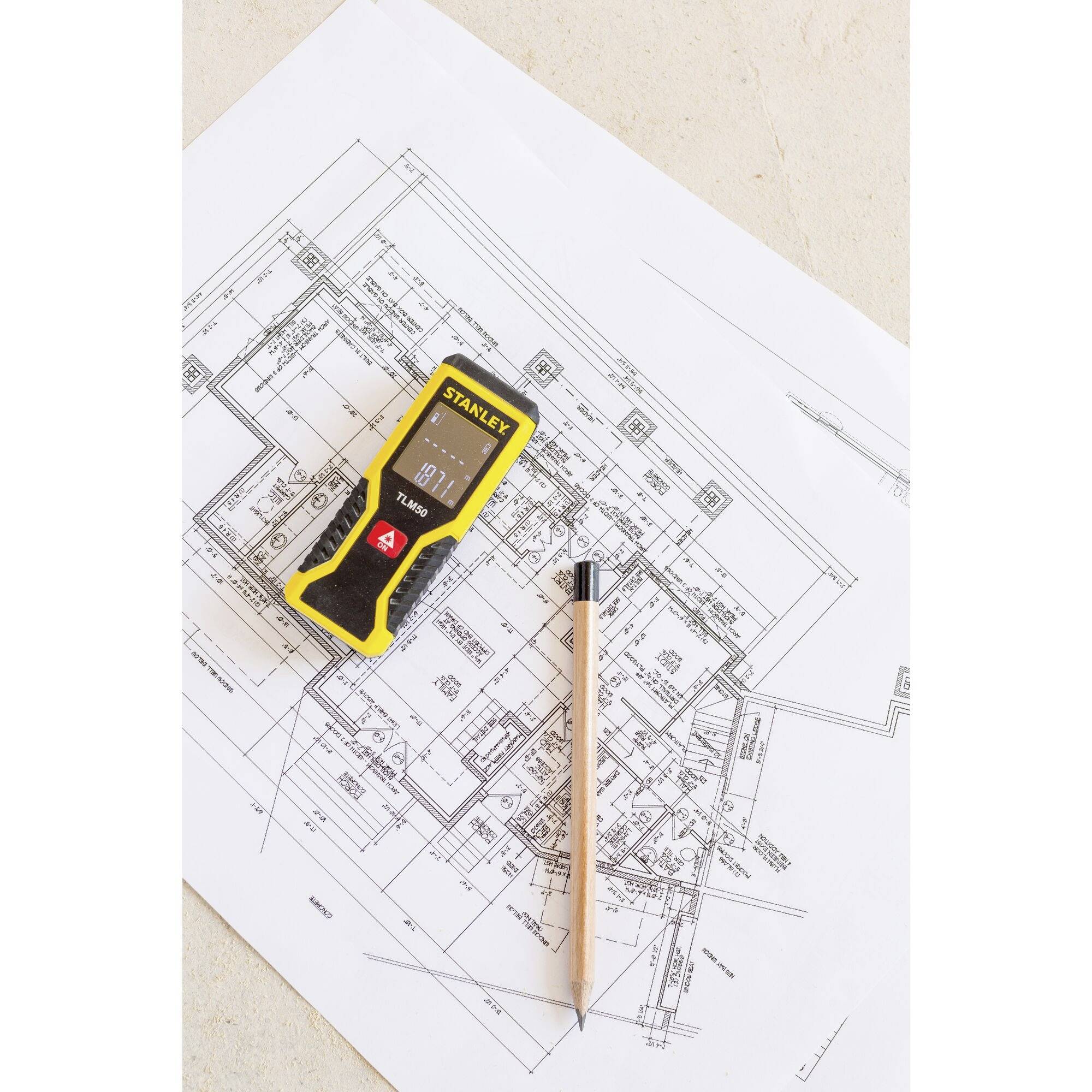 Ein Laser-Entfernungsmesser und ein Bleistift liegen auf einem Architekturplan. Der Plan zeigt detaillierte Grundrisse eines Gebäudes.