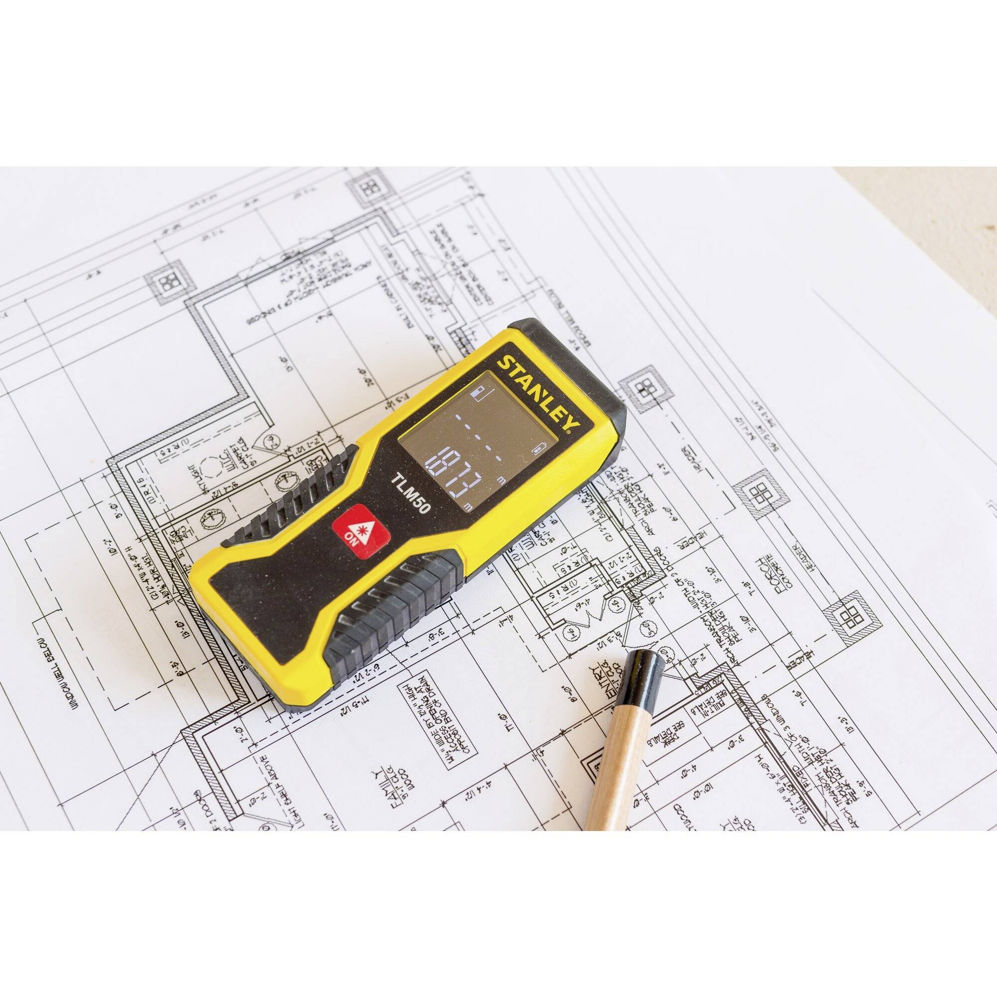 Ein gelbes Messgerät liegt auf einem Architekturplan daneben ein Bleistift. Das Display zeigt '1.79'. Der Fokus liegt auf präzisem Messen.