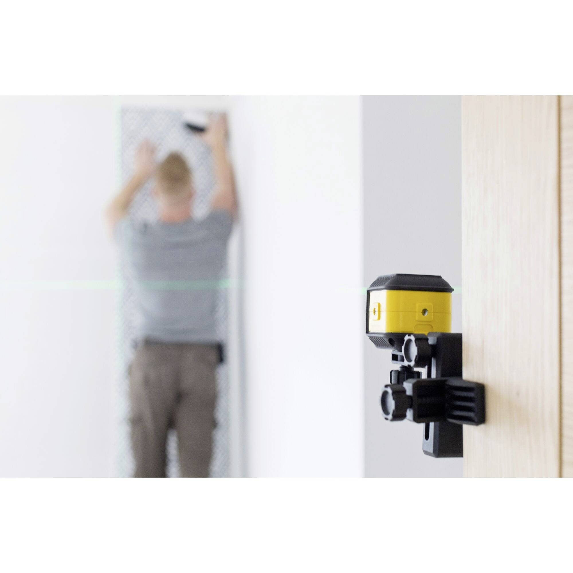 Eine Person nivelliert eine Wand mit einem Laserwerkzeug. Das gelbe Lasergerät sorgt für präzise Ausrichtung beim Bohren oder Montieren.