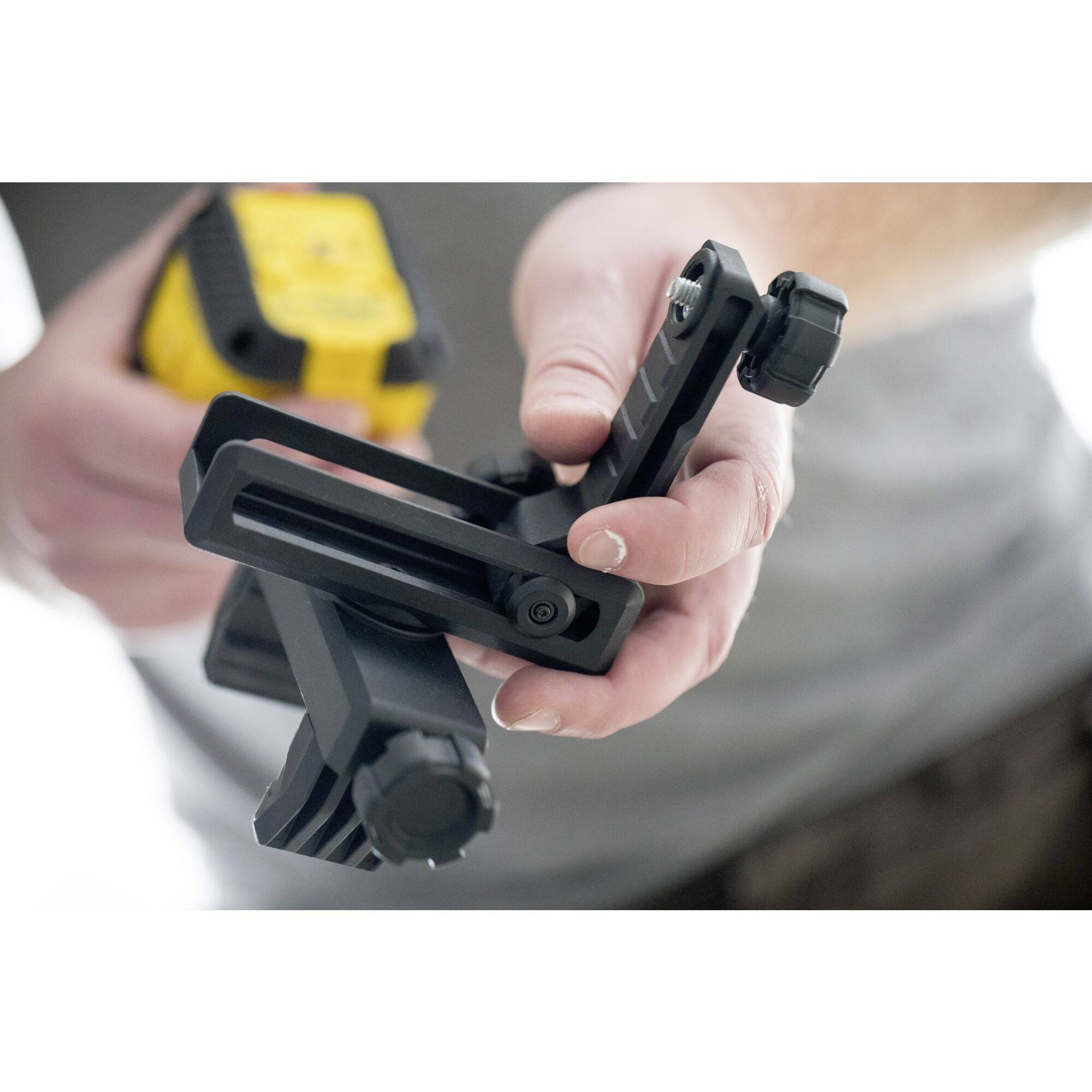 Eine Person hält ein Kamerazubehör aus schwarzem Metall in der Hand, bereit zur Montage oder Justierung. Hintergrund unscharf.