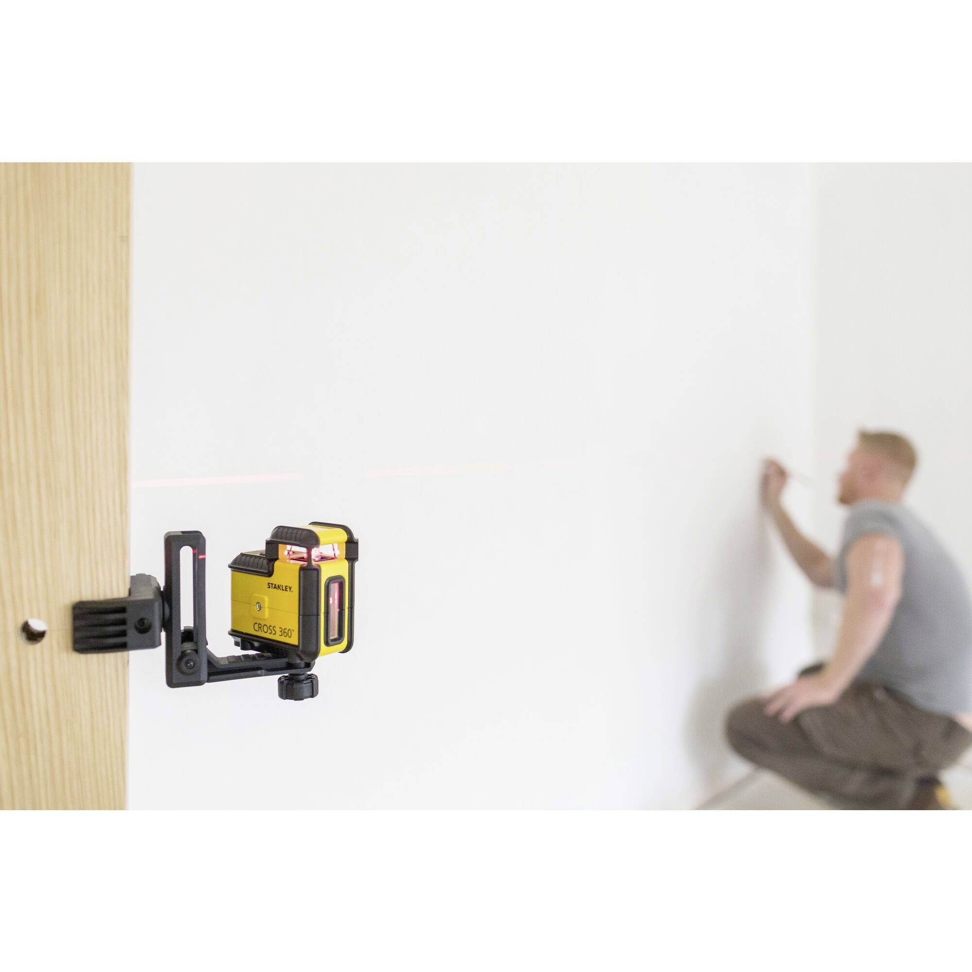 Eine Person richtet mithilfe eines gelben Lasernivelliergeräts eine gerade Linie an einer weißen Wand aus.