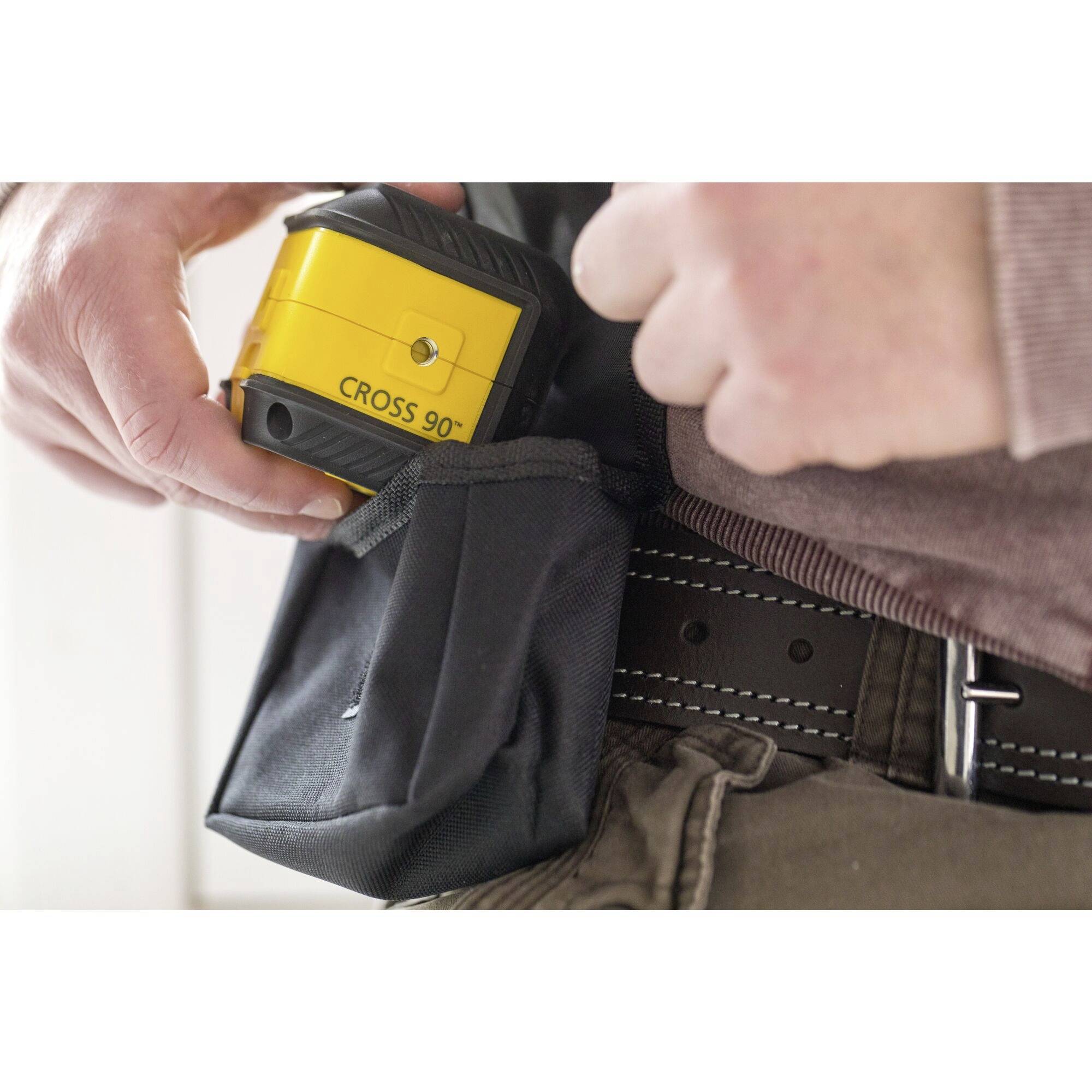 Ein gelbes Kreuzlinienlasergerät wird in eine schwarze Werkzeugtasche gesteckt. Die Hände einer Person sind zu sehen.