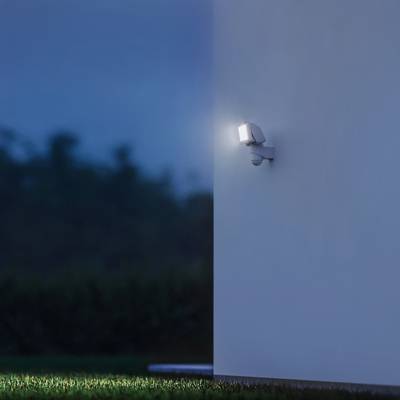 Außenwand mit leuchtendem Flutlicht in der Abenddämmerung, beleuchtet einen Teil des Rasens.
