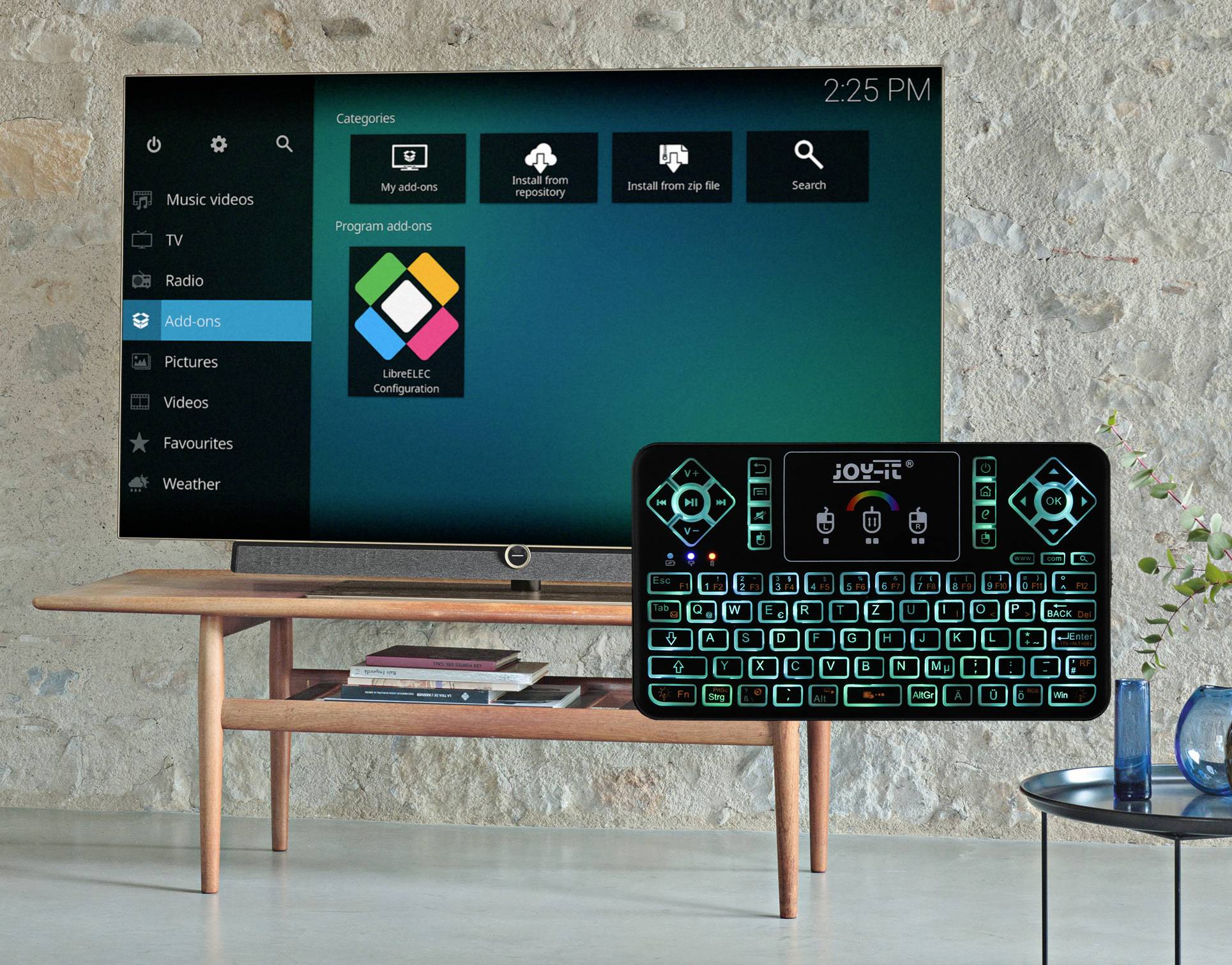 'Smart-TV-Bildschirm zeigt Menü mit Optionen wie Musik, Videos und Radio. Darunter Tisch, darüber schwebende Tastatur mit leuchtenden Tasten.'