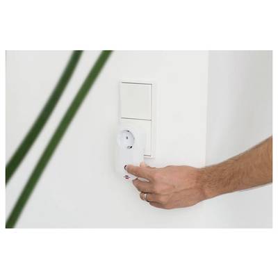 Hand, die ein Gerät in eine weiße Wandsteckdose neben einer Schalterplatte einsteckt.