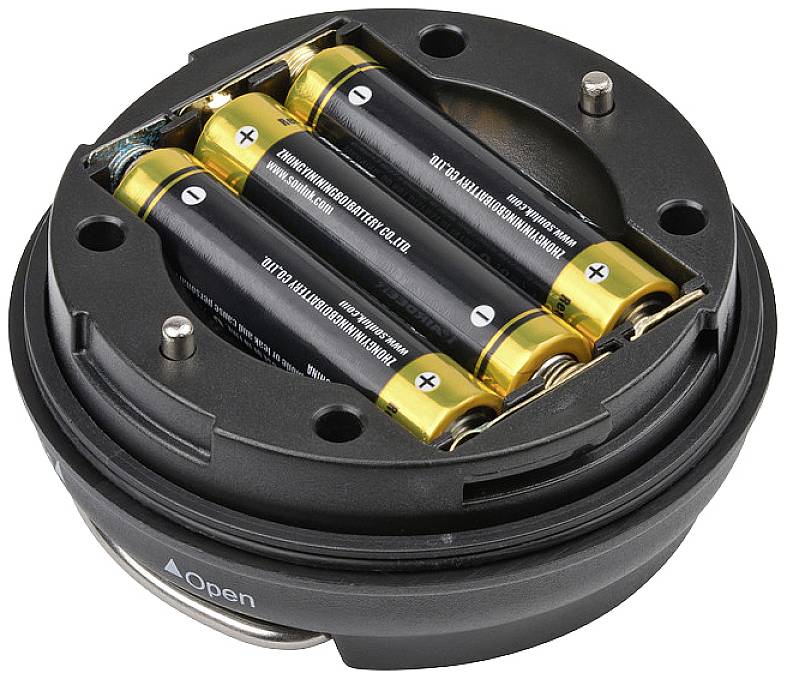 Batteriefach mit drei AA-Batterien in einem runden schwarzen Gerät geöffnet, inklusive 'Open'-Kennzeichnung für einfache Entnahme.