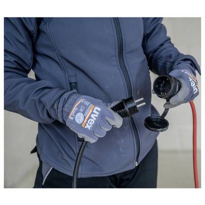 Person in Handschuhen und Jacke inspiziert einen Stromstecker und eine Buchse mit einem roten Kabel angeschlossen.