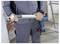 Person holding a cordless caulking gun, wearing work gear, standing at a construction site with exposed brick and ladder nearby.