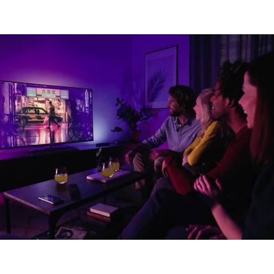 Eine Gruppe von vier Personen sitzt auf einem Sofa und schaut gemeinsam einen Film auf einem großen Fernseher in einem dunklen Zimmer.