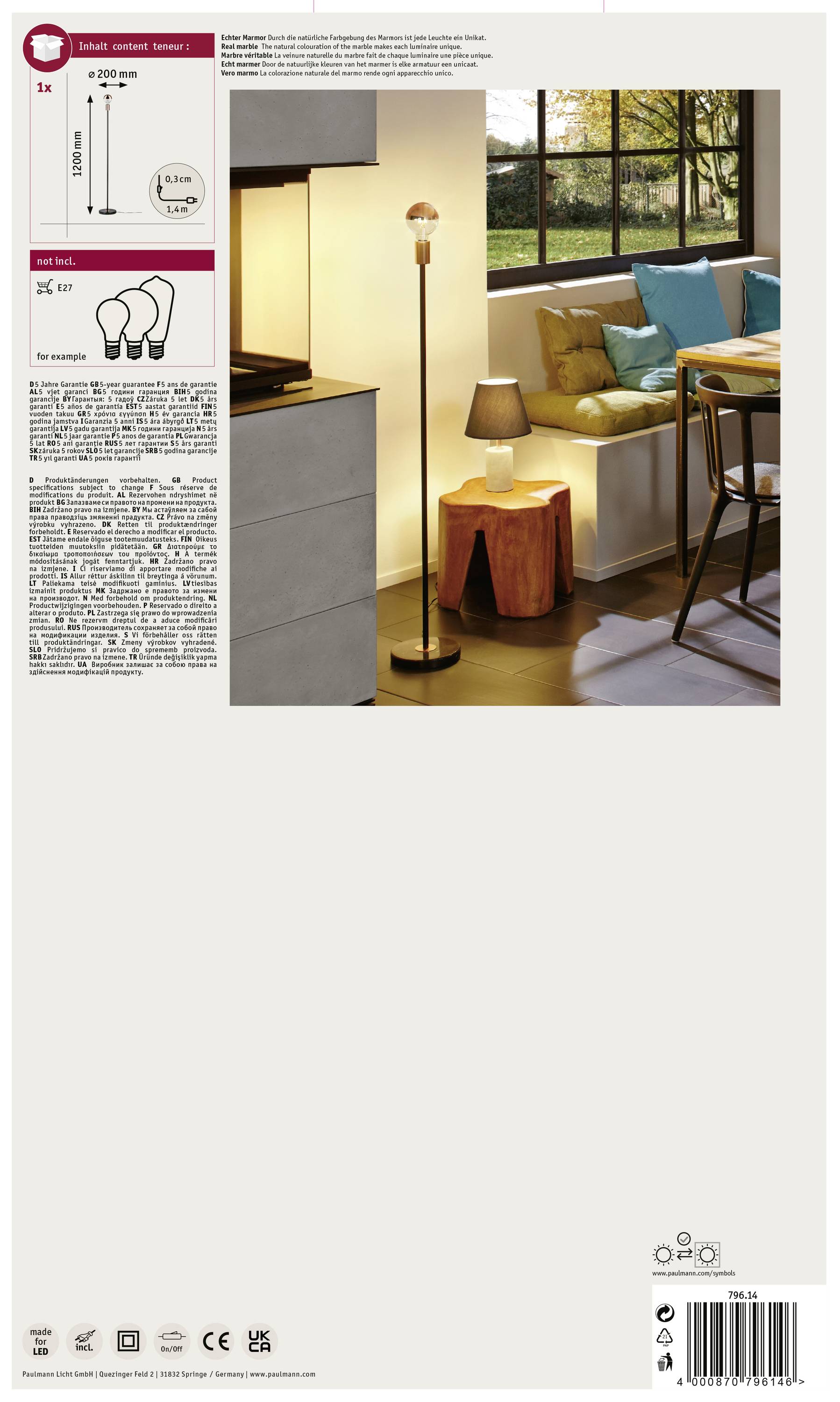 Eine Stehlampe steht in einem gemütlichen Wohnzimmer neben einem Tisch mit Lampe. Im Hintergrund sind ein Sofa und ein großes Fenster zu sehen.