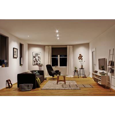 Ein modernes Wohnzimmer mit Holzboden, einem schwarzen Sofa, Sessel, Teppichen und Pflanzen. Kunstwerke an den Wänden, dezente Beleuchtung.