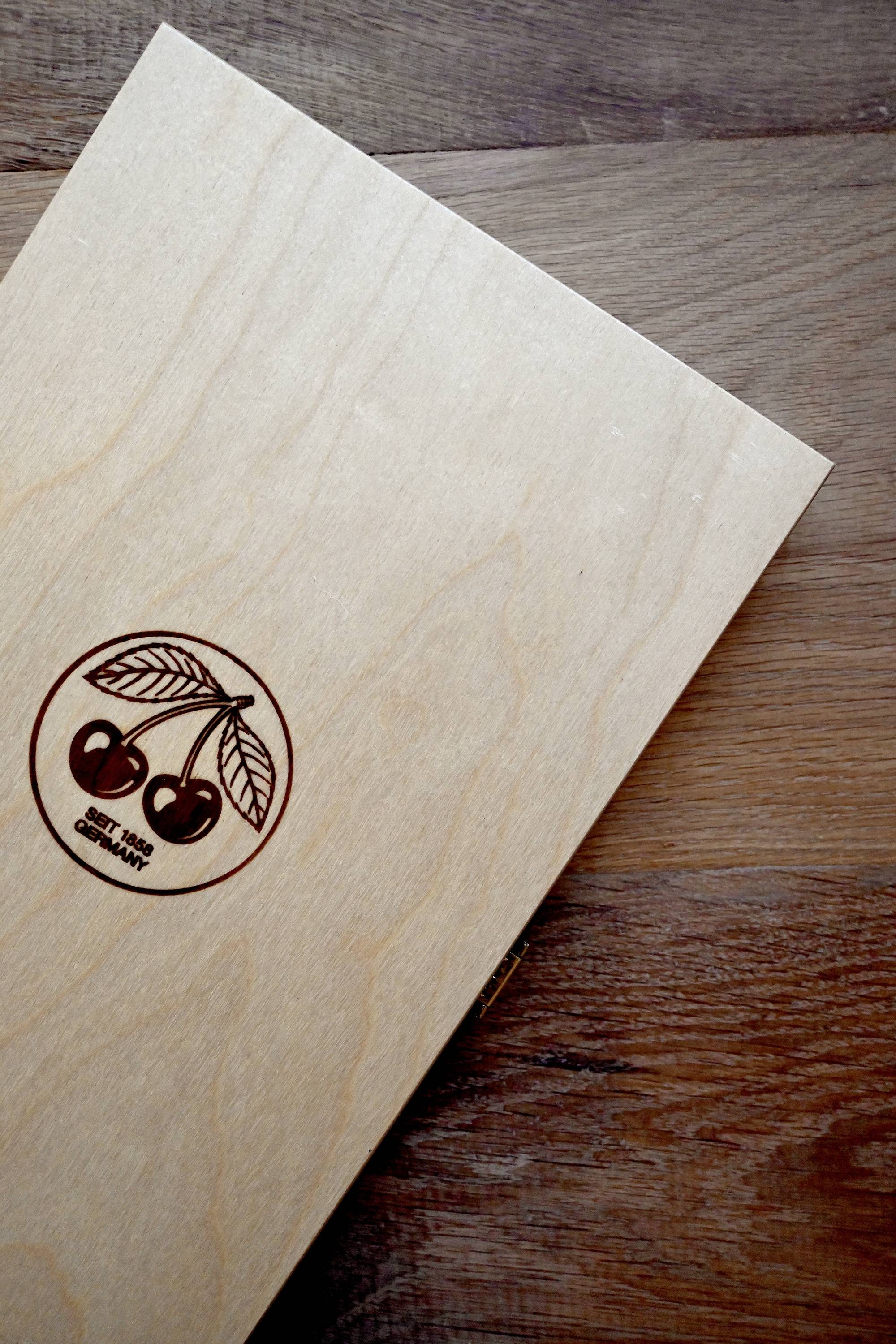 Ein rechteckiges Holzbrett mit einem aufgedruckten Kirsch-Logo am Rand liegt auf einem Tisch mit Holzmaserung.