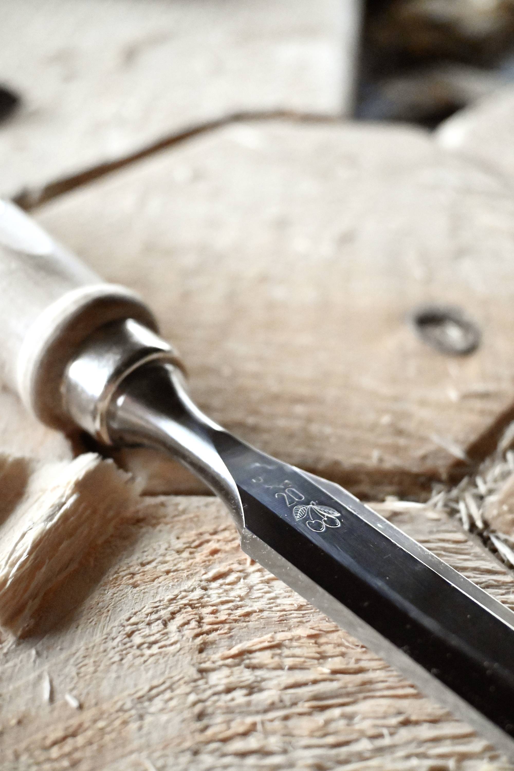 Holzschnittdetail: Nahaufnahme eines Schnitzmessers auf einem Holzblock. Das Messer zeigt feine Schnitzarbeiten im Holz.