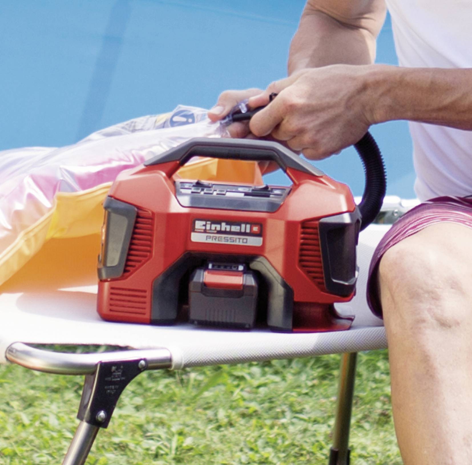 Eine Person pumpt eine aufblasbare Matratze mit einer roten elektrischen Luftpumpe auf, die auf einem Tisch liegt.