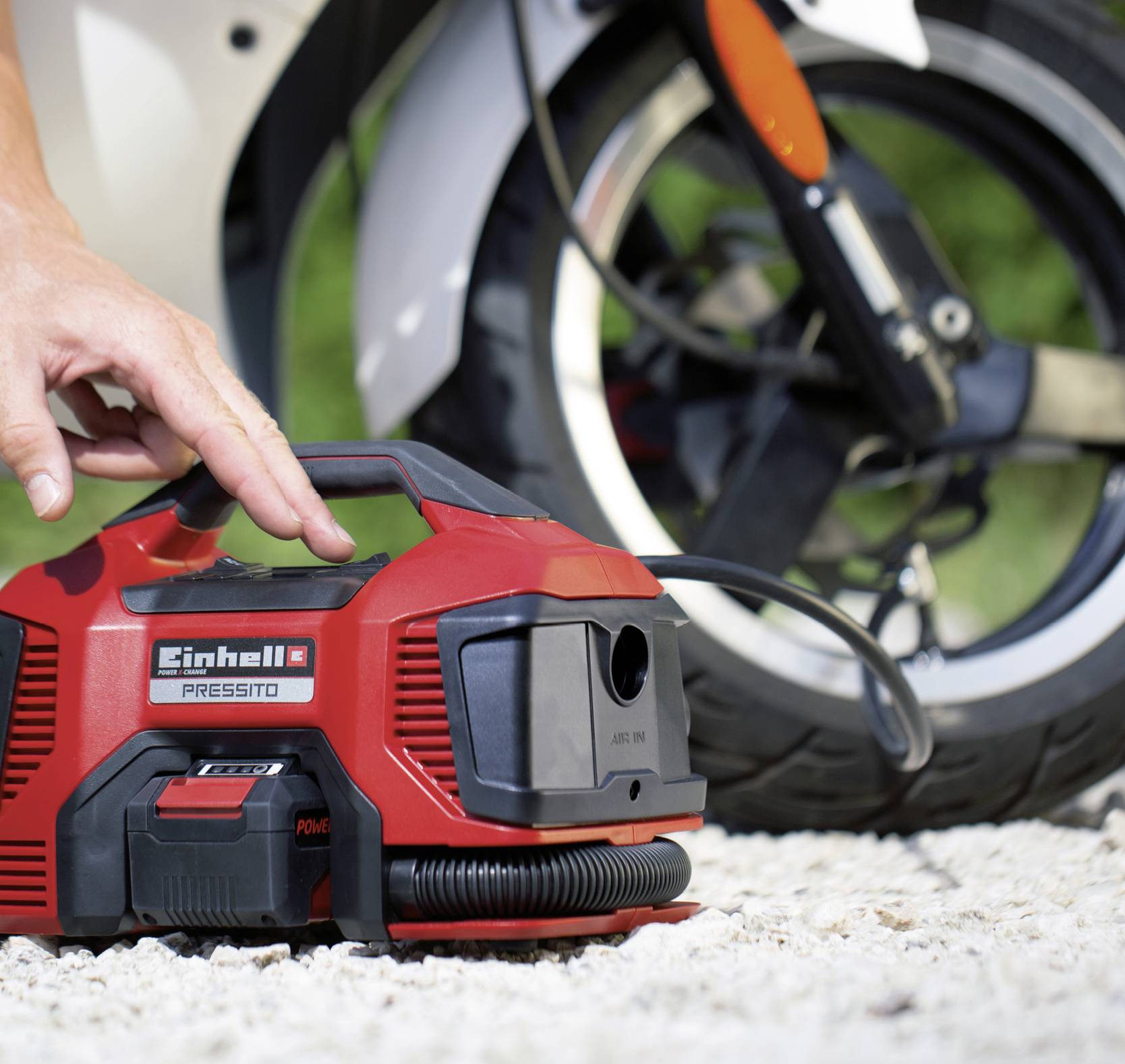 Eine Person benutzt eine tragbare Luftkompressor-Pumpe, um die Reifen eines Motorrads im Freien auf Kiesboden aufzupumpen.