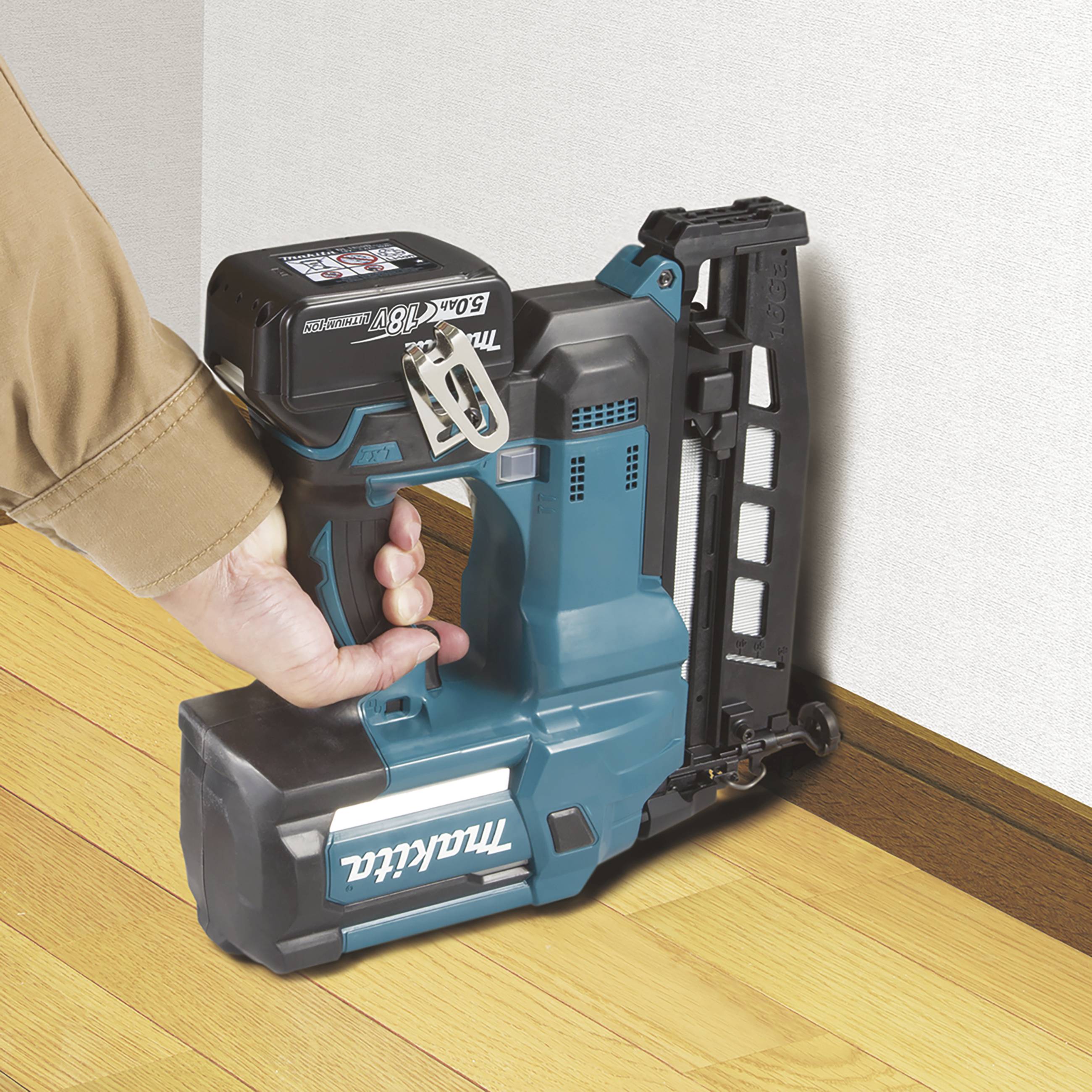 Eine Person hält ein blaues Elektrowerkzeug an der Wand, um Holzbodenleisten präzise zu befestigen.