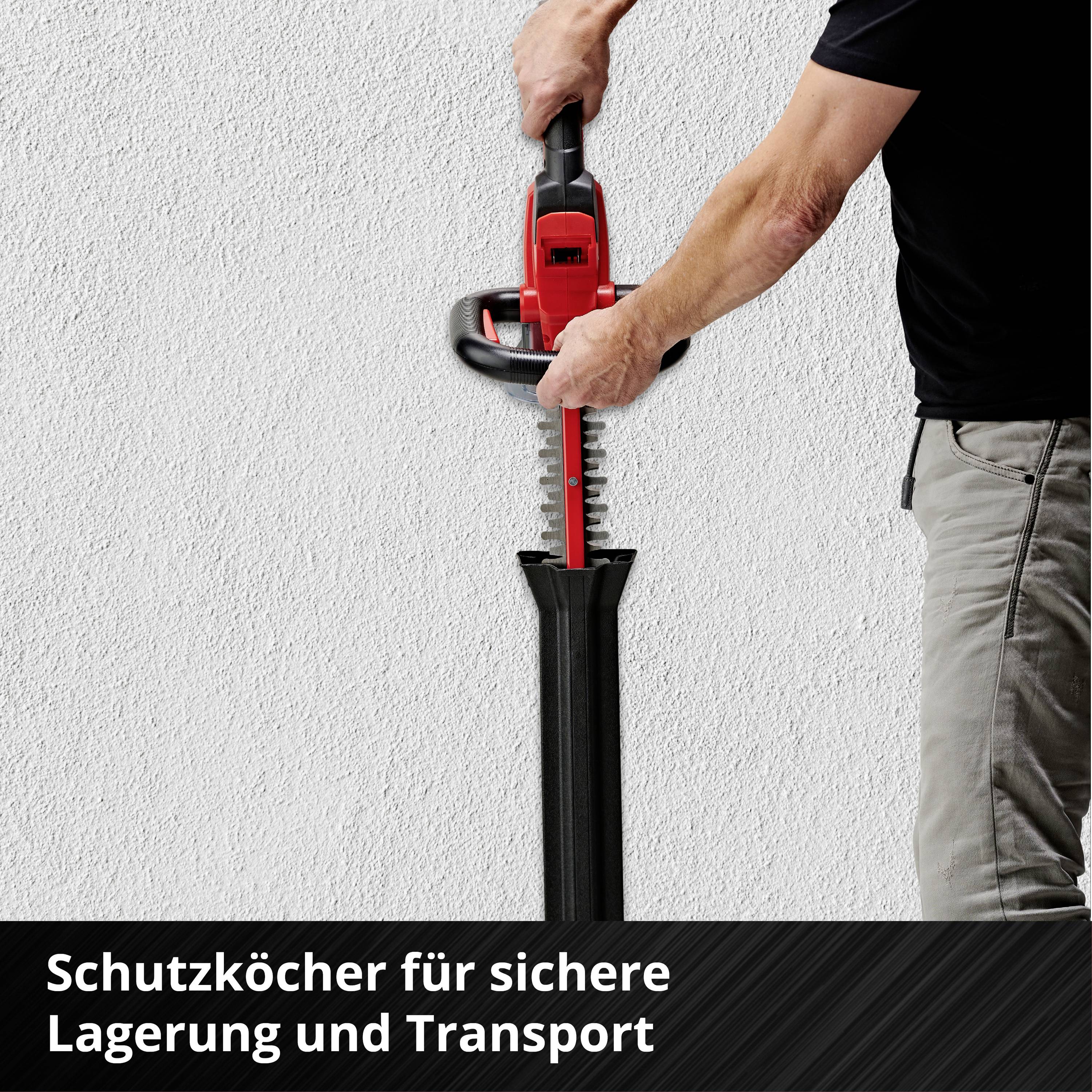 Mann hält eine rote Heckenschere an einer weißen Wand. Text unten: 'Schutzköcher für sichere Lagerung und Transport'.
