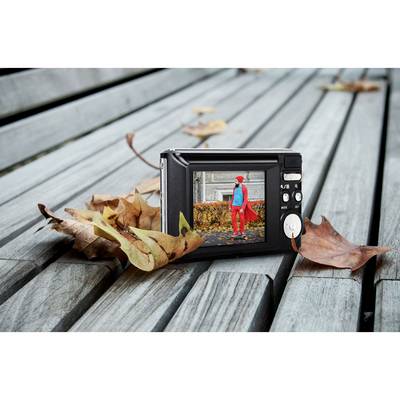 Eine digitale Kamera liegt auf einem Holztisch. Auf dem Bildschirm ist eine Person in roter Jacke und Mütze auf einem Parkweg zu sehen.