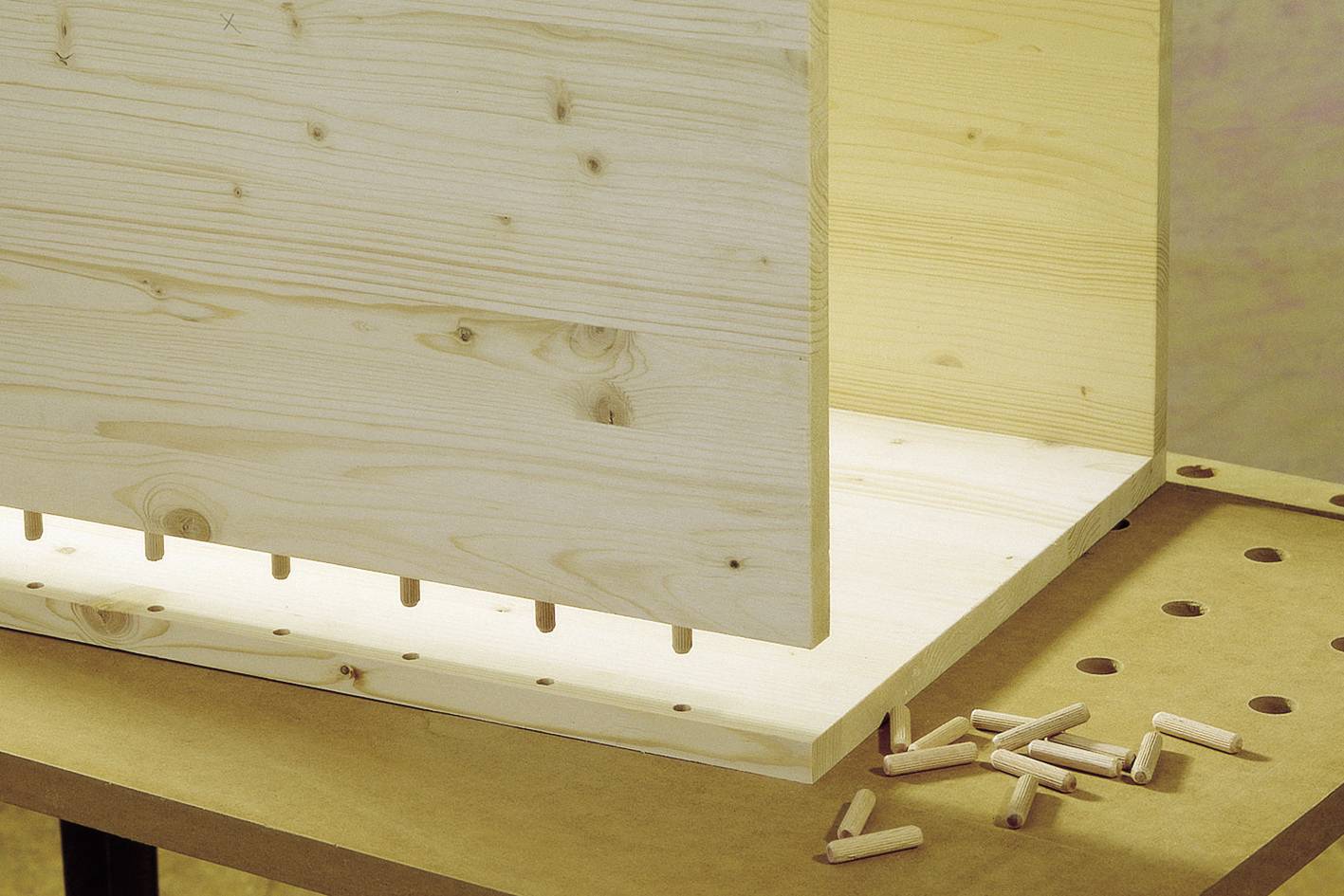 Ein offener Holzschrank mit Dübeln in den Seiten, auf einem Tisch liegend, zeigt den Zusammenbauprozess von Holzmöbeln.