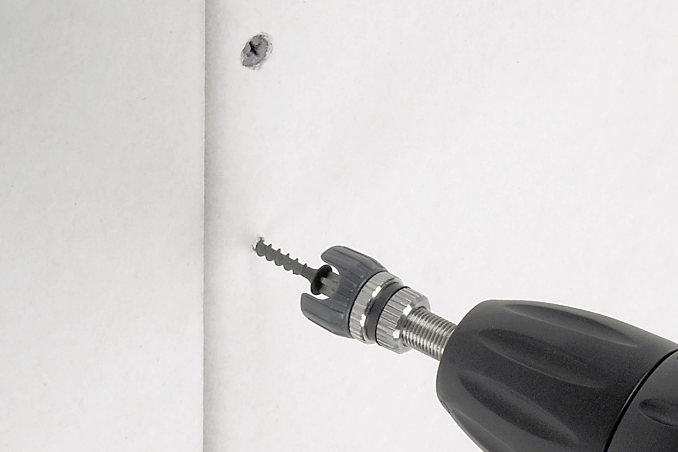 Elektrische Säge schneidet kreisförmiges Loch in weiße Wand. Zwei Schraubendübel sind sichtbar.