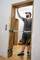 Ein Mann montiert einen Türrahmen aus Holz in einem Haus. Er trägt Arbeitskleidung und Mütze und verwendet Montagehilfen.