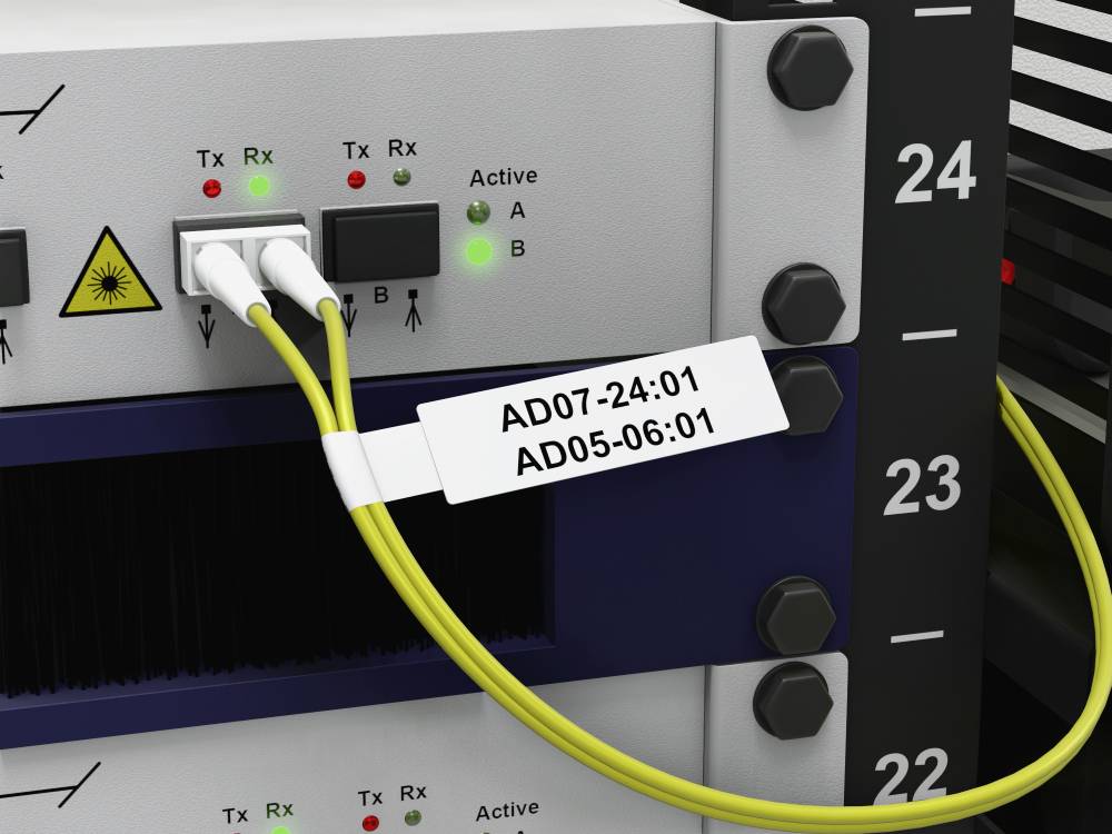 'Netzwerk-Switch mit zwei gelben Glasfaserkabeln, die in die Ports A und B eingesteckt sind. Etikett zeigt AD07-24:01 und AD05-06:01.'