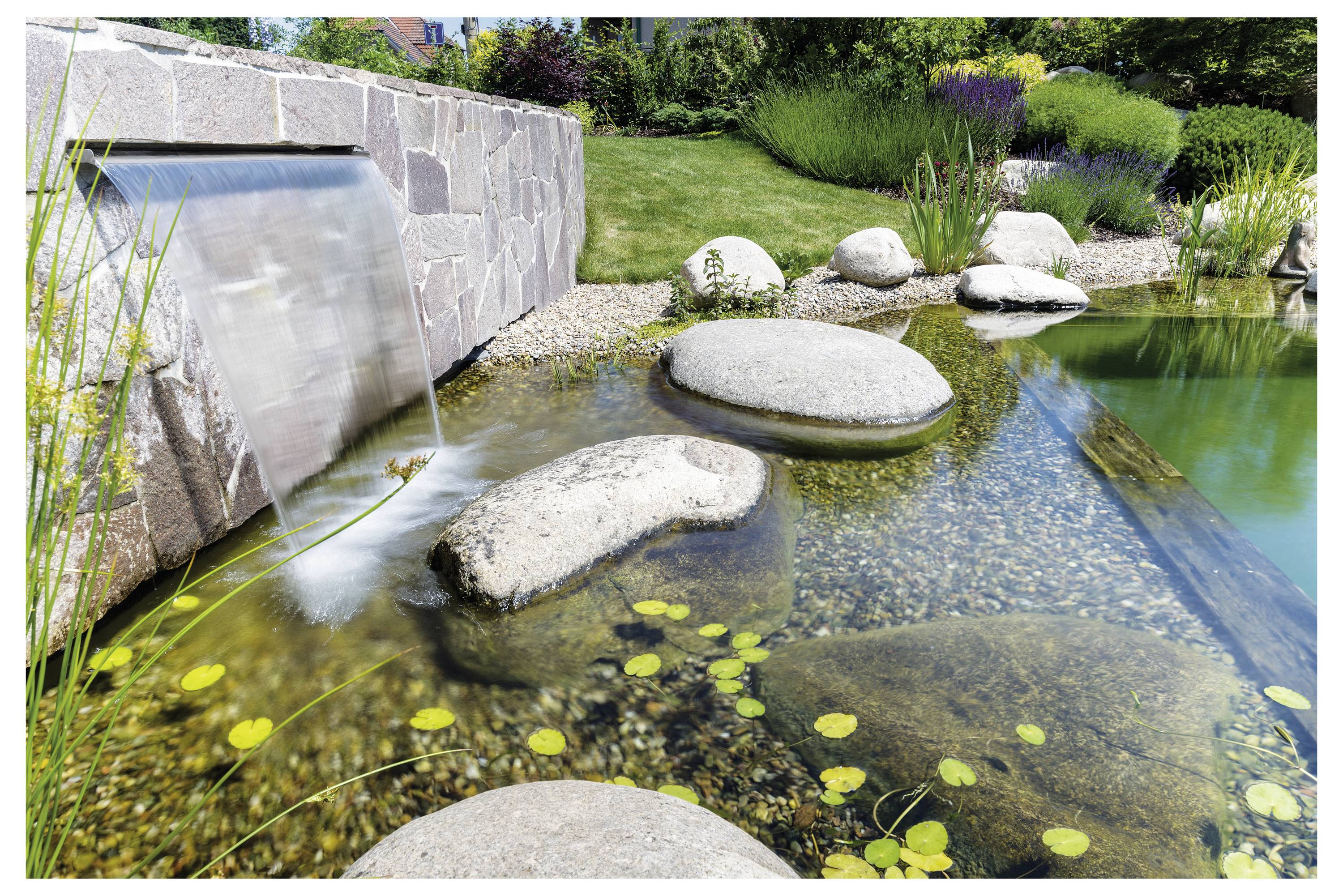 Ein ruhiger Gartenweiher mit herabfallenden Wasserfällen, glatten Steinen und üppiger Vegetation. Klares Wasser fließt über Felsen, umgeben von Pflanzen.