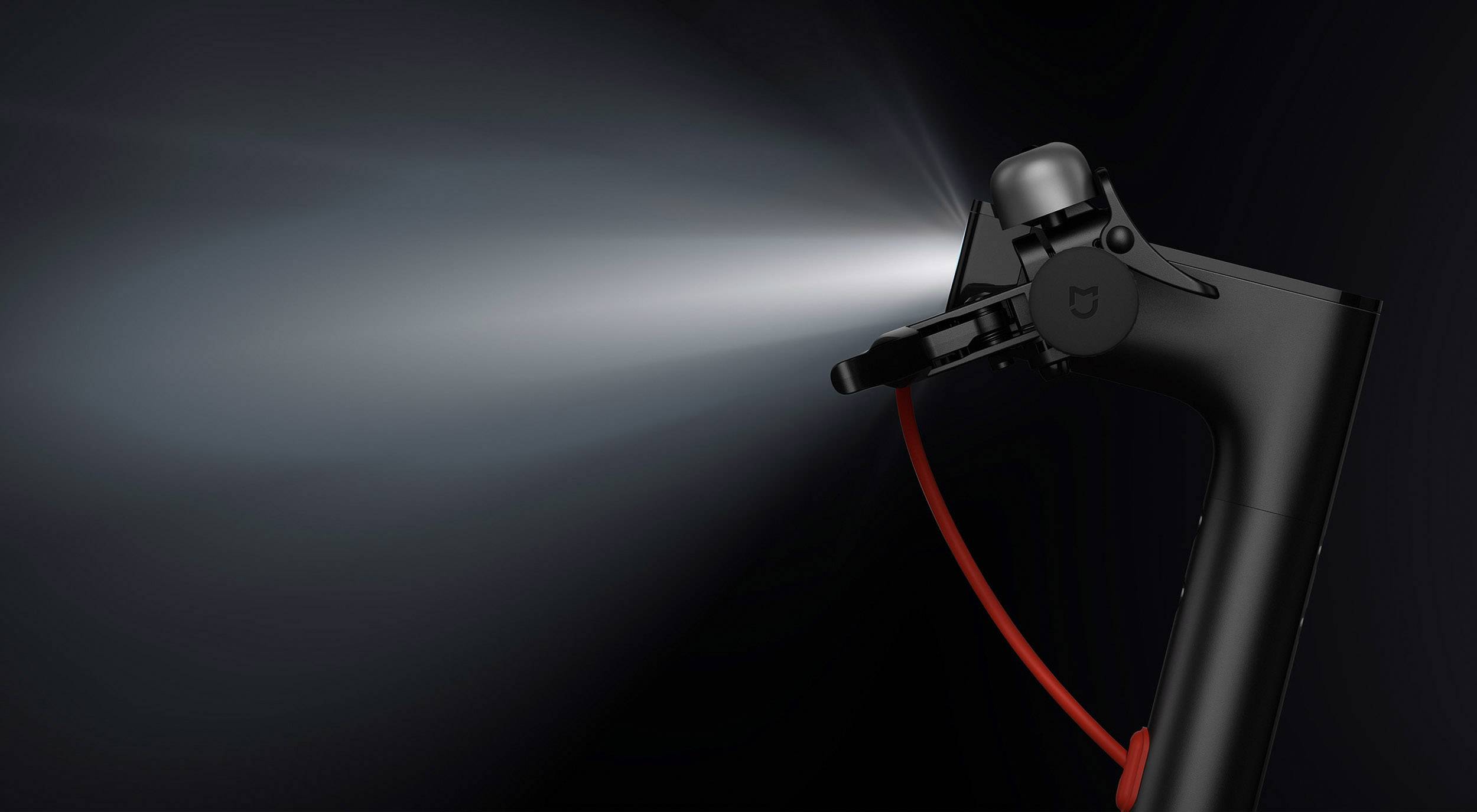 Ein schwarzer Rollerlenker mit eingebautem Frontlicht in Betrieb. Das Licht leuchtet hell nach vorne, Kabel in Rot als Akzent.