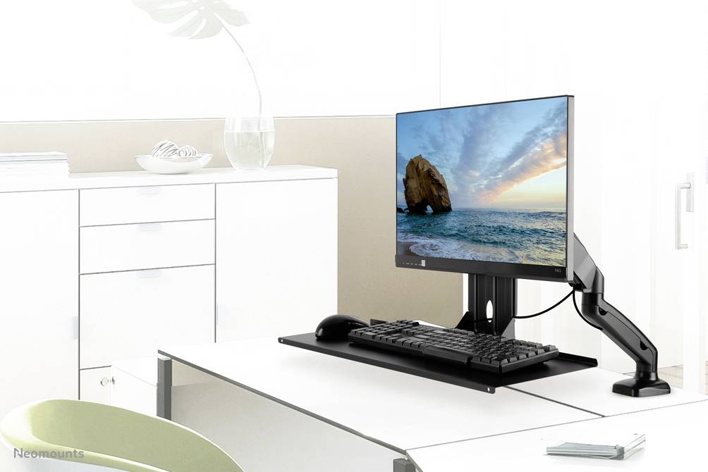 Ein Schreibtisch mit einem Monitorarm, der einen Monitor mit einem Strandbild hält. Daneben befinden sich eine Tastatur und eine Maus.