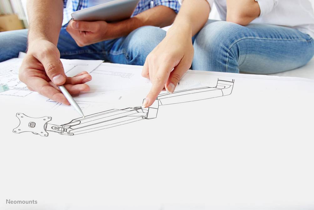 Zwei Personen diskutieren ein technisches Design auf einem Papier. Eine Person zeigt darauf, während die andere eine Zeichnung hält.