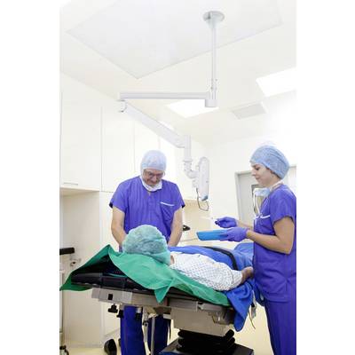 Ein Patient liegt auf einem OP-Tisch, während zwei Chirurgen in blauen Kitteln und OP-Mützen Vorbereitungen im Operationssaal treffen.