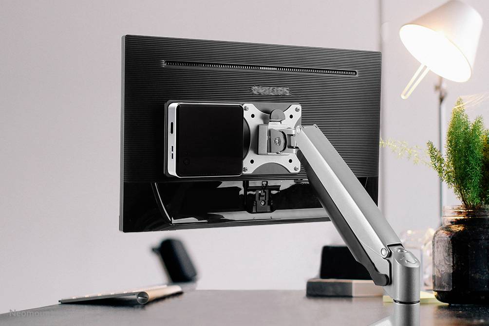Ein Smartphone ist auf der Rückseite eines Computermonitors mit einer speziellen Halterung angebracht, auf einem Schreibtisch.