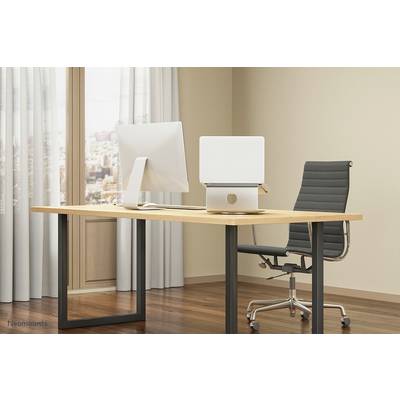 Moderner Schreibtisch mit Computer und ergonomischem Stuhl in einem hellen Büro mit Fenster.