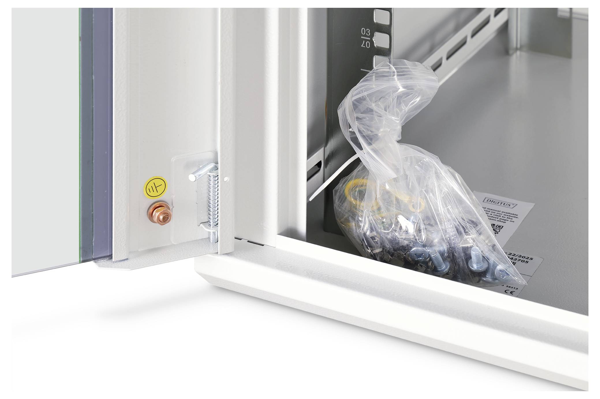 Eine durchsichtige Tüte mit Schrauben und einem Unterlegscheiben-Set wird in einem offenen weißen Schrank platziert, wobei Verpackungsetiketten im Hintergrund sichtbar sind.