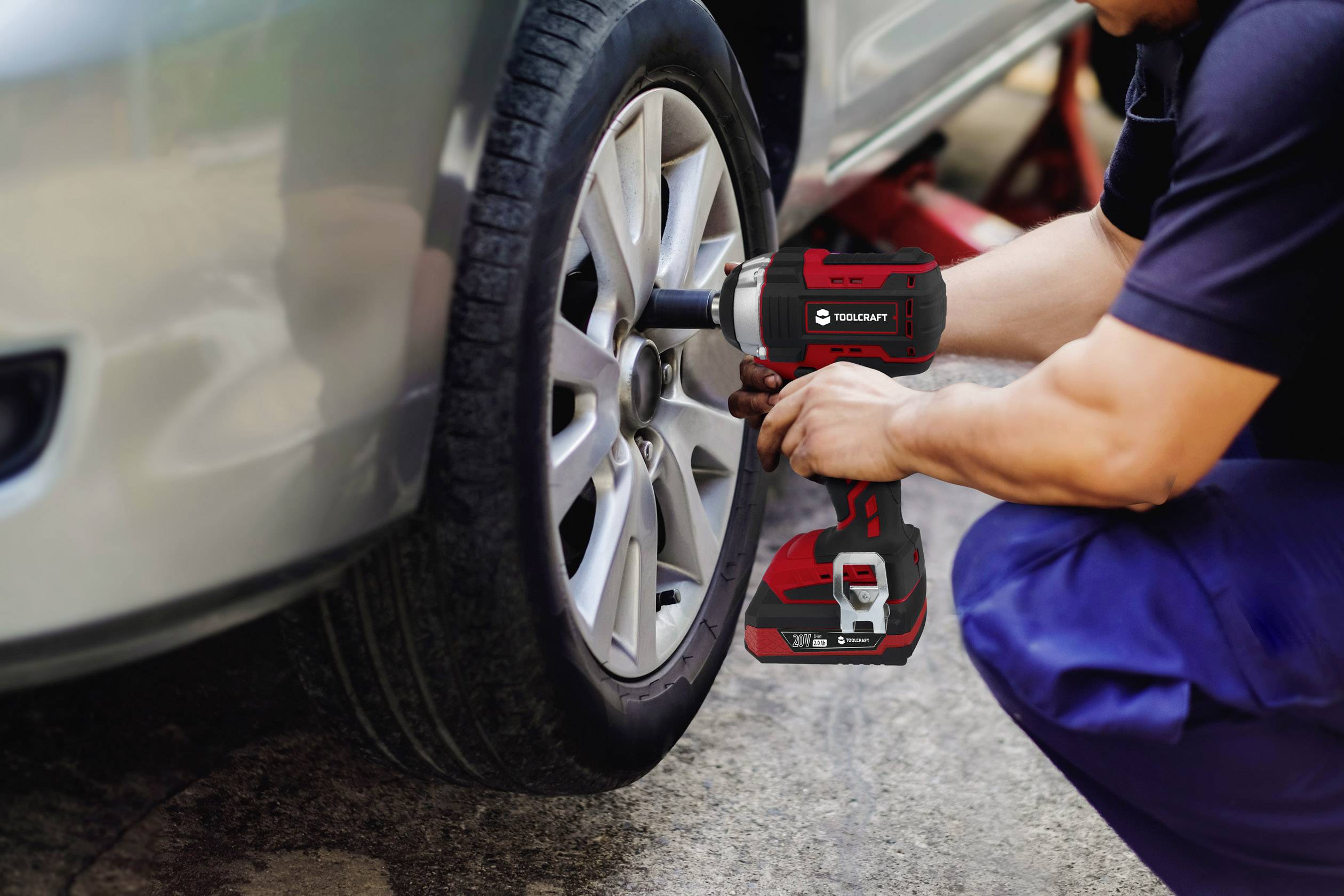 Eine Person wechselt mit einem Elektrowerkzeug einen Reifen an einem Auto. Das Auto steht aufgebockt auf einem Wagenheber.