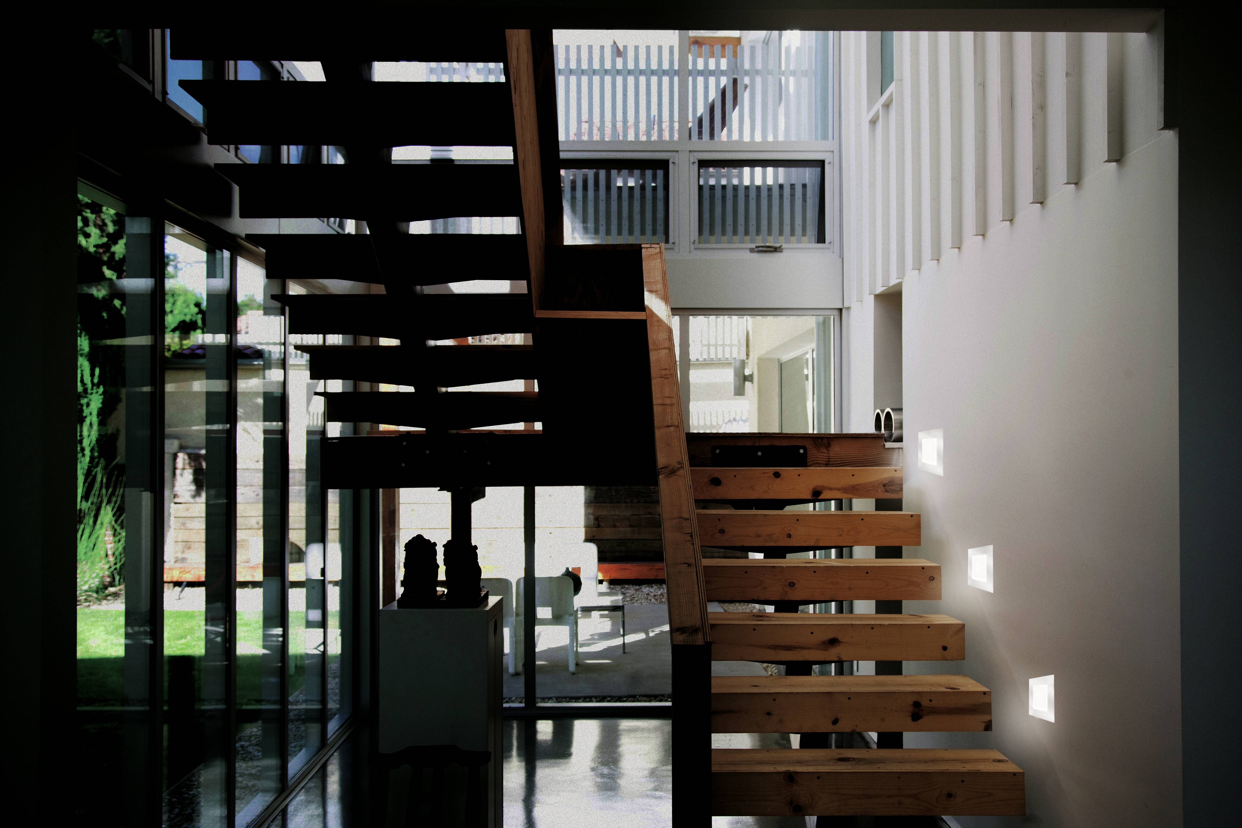Moderne Holztreppe in einem Gebäude mit Glaswänden, die viel Licht durchlässt. Schatten und Licht erzeugen ein interessantes Muster im Innenraum.