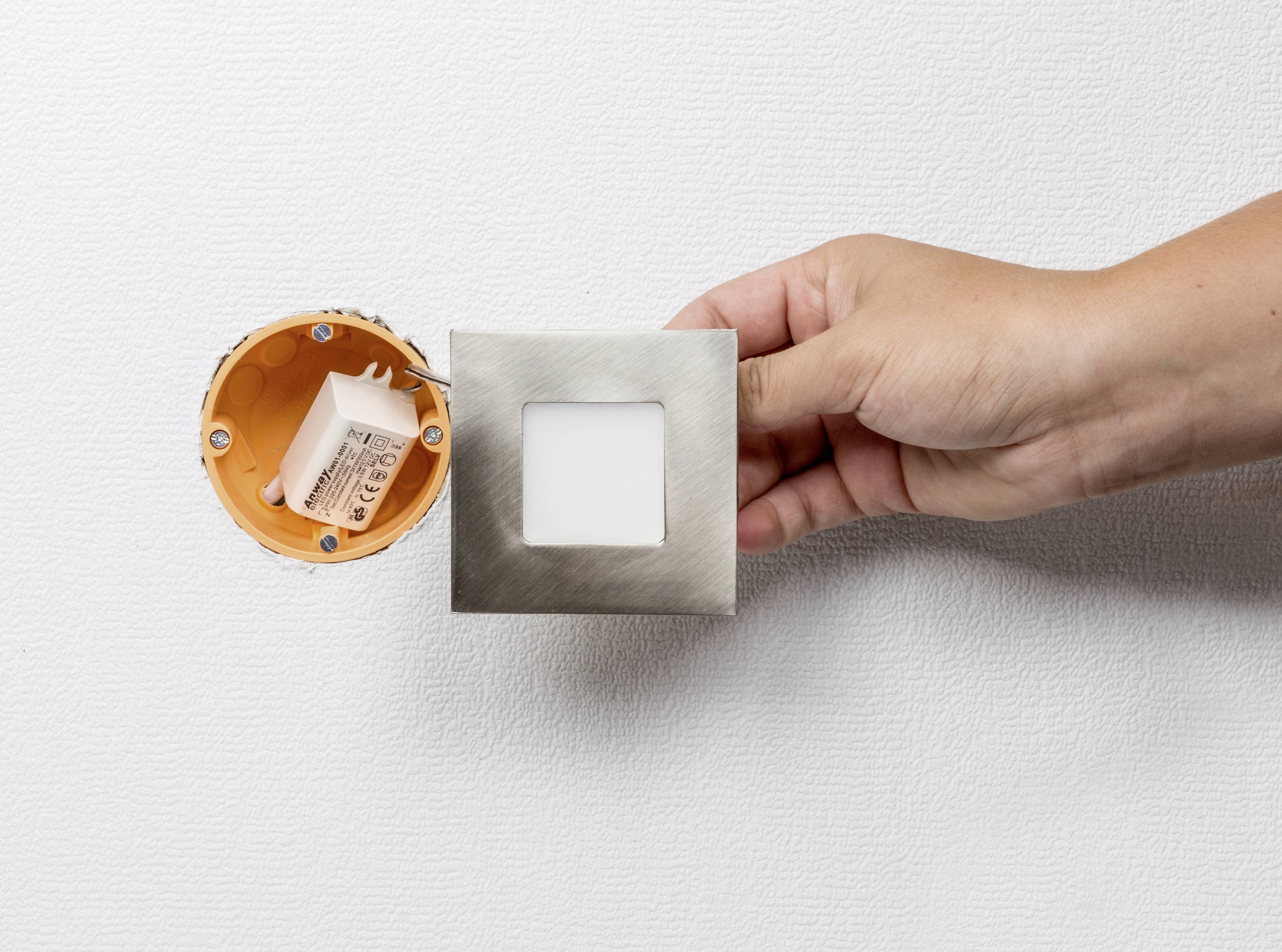 'Eine Hand montiert ein quadratisches LED-Licht in eine runde Wandöffnung.'