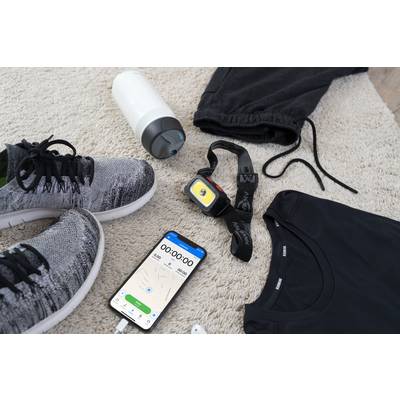 Sportbekleidung und Zubehör liegen auf einem Teppich: Schuhe, Trinkflasche, Kopfhörer, Laufuhr, Trainingshose und ein Smartphone mit offener Fitness-App.