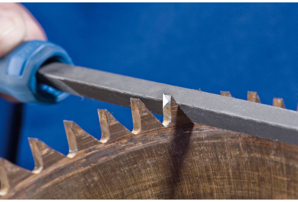 Person schleift mit Feile die Zähne einer Kreissäge. Nahaufnahme zeigt die sorgfältige Handarbeit an der Metallklinge.