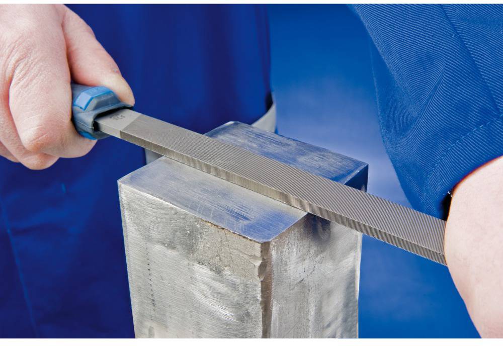 Eine Person feilt mit einer Metallfeile die Kante eines Metallblocks. Die Szene zeigt den Fokus auf handwerkliche Präzision.