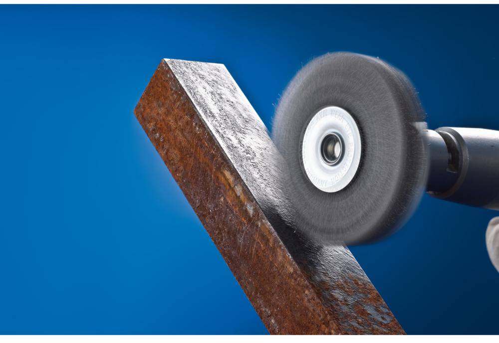 Eine Poliermaschine bearbeitet einen rostigen Metallbalken. Der Hintergrund ist blau.