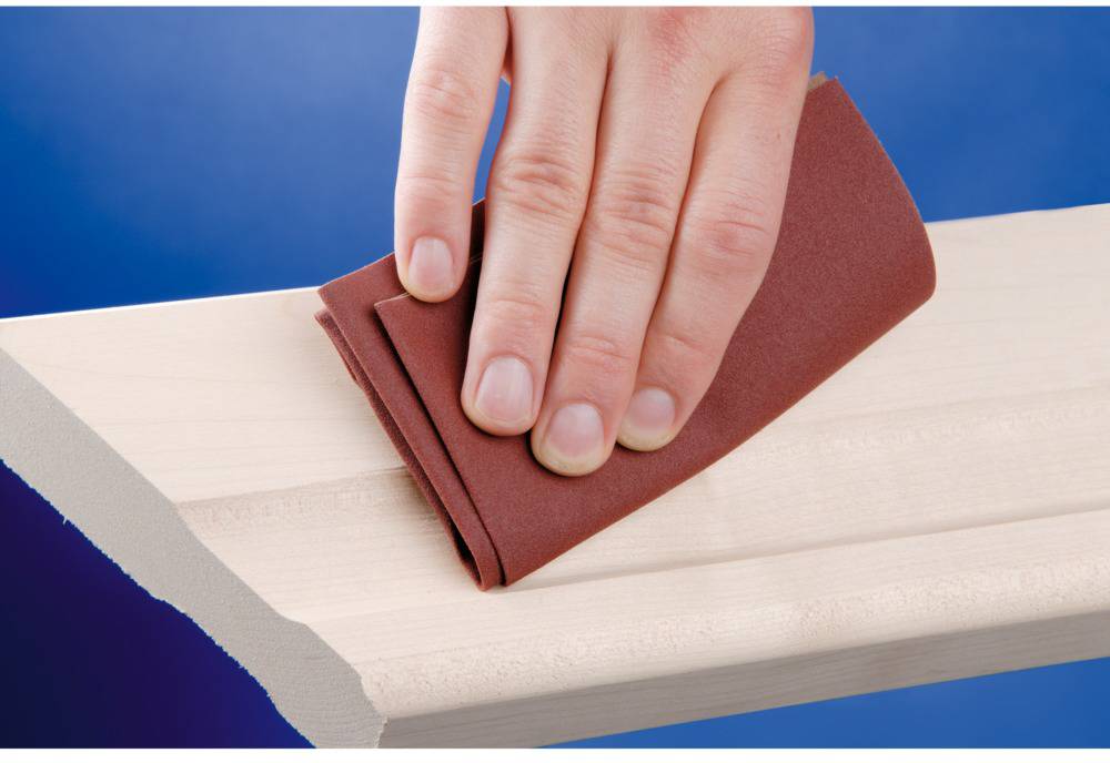 Eine Hand schleift mit einem roten Schleifpapier ein helles Holzbrett.