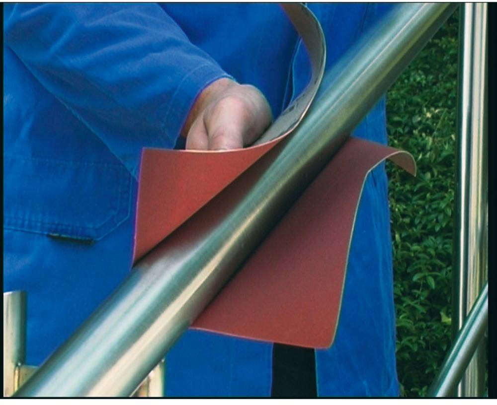 Eine Person in blauer Arbeitskleidung schleift ein Metallgeländer mit rotem Schleifpapier.