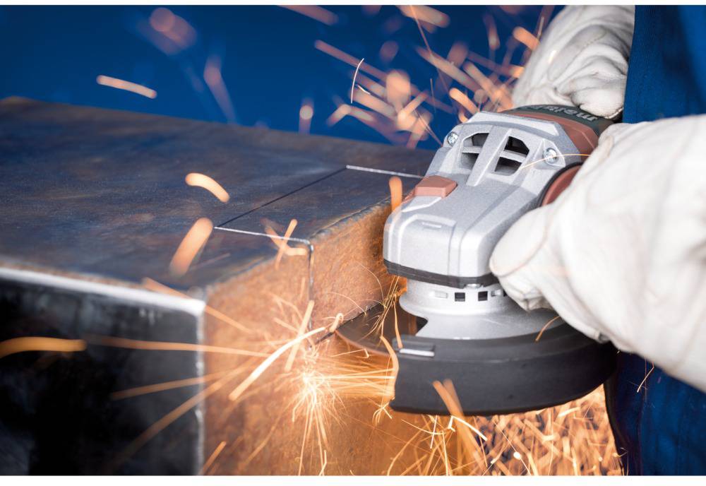 Ein Handwerker schleift die Kante eines Metallbalkens mit einem Winkelschleifer, Funken sprühen von der Bearbeitungsstelle.