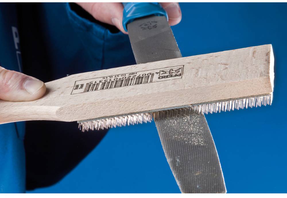 Eine Person schärft ein Messer mit einem Schleifbürstenblock. Der Holzgriff der Bürste trägt einen Barcode-Etikett.