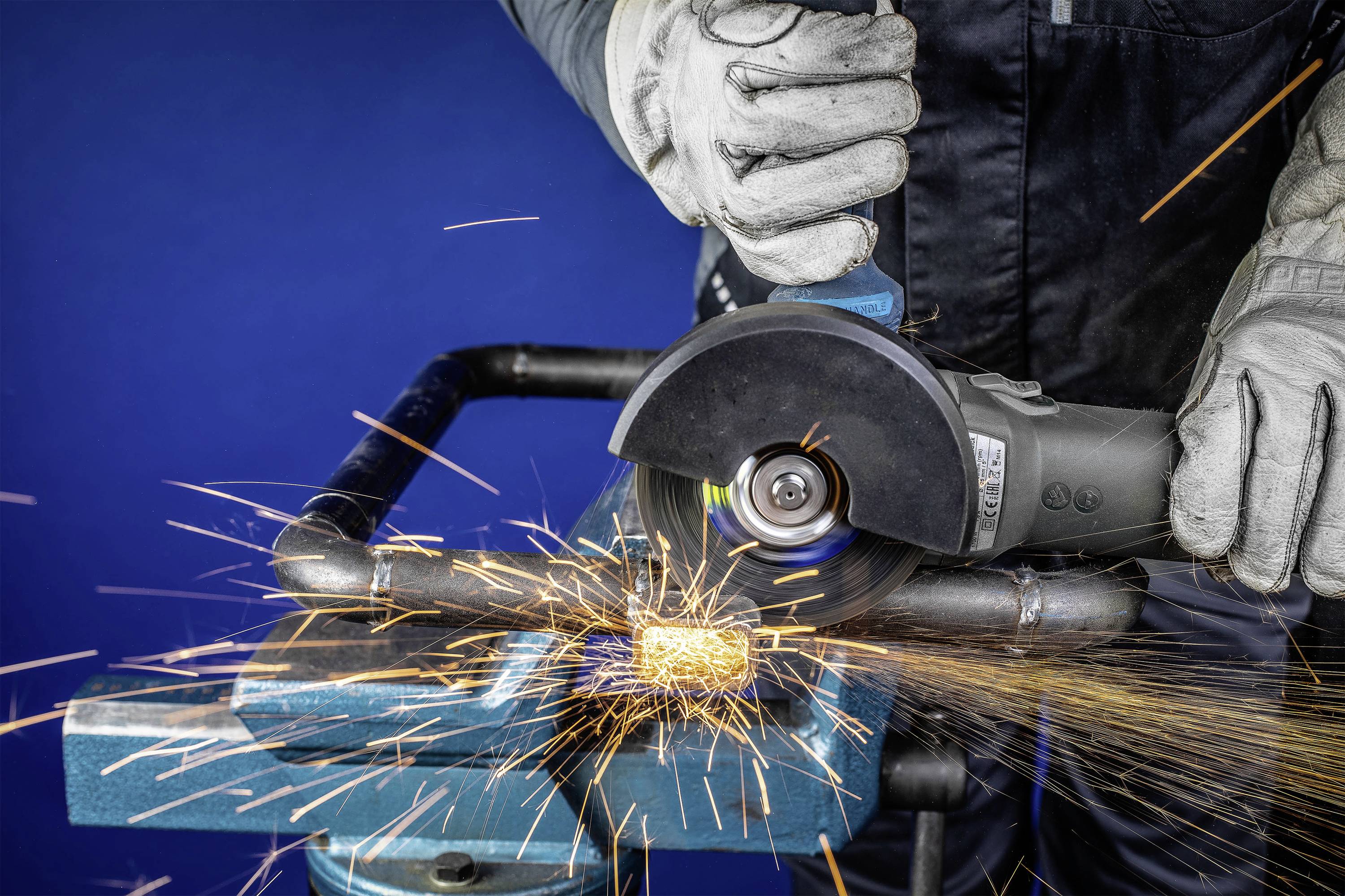 Ein Arbeiter mit Schutzhandschuhen schneidet mit einer elektrischen Schleifmaschine Metall, während Funken sprühen.