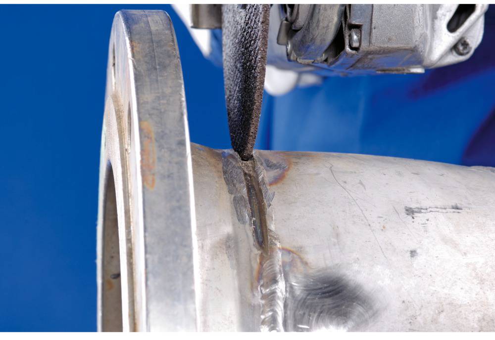 Ein Metallstück wird mit einem Schleifgerät bearbeitet. Die Schleifscheibe ist nah an der Schweißnaht des Werkstücks positioniert.