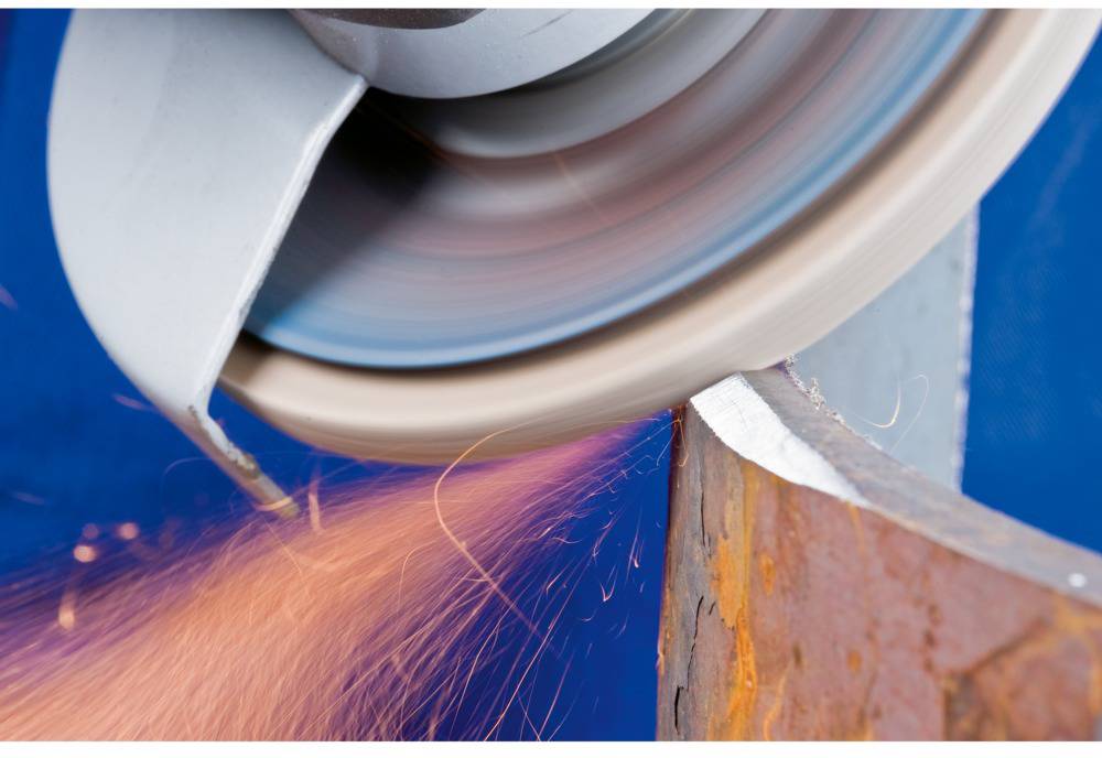 Schleifscheibe bearbeitet Metallstück, erzeugt Funkenflug. Nahaufnahme zeigt industrielle Metallverarbeitung bei hoher Geschwindigkeit.