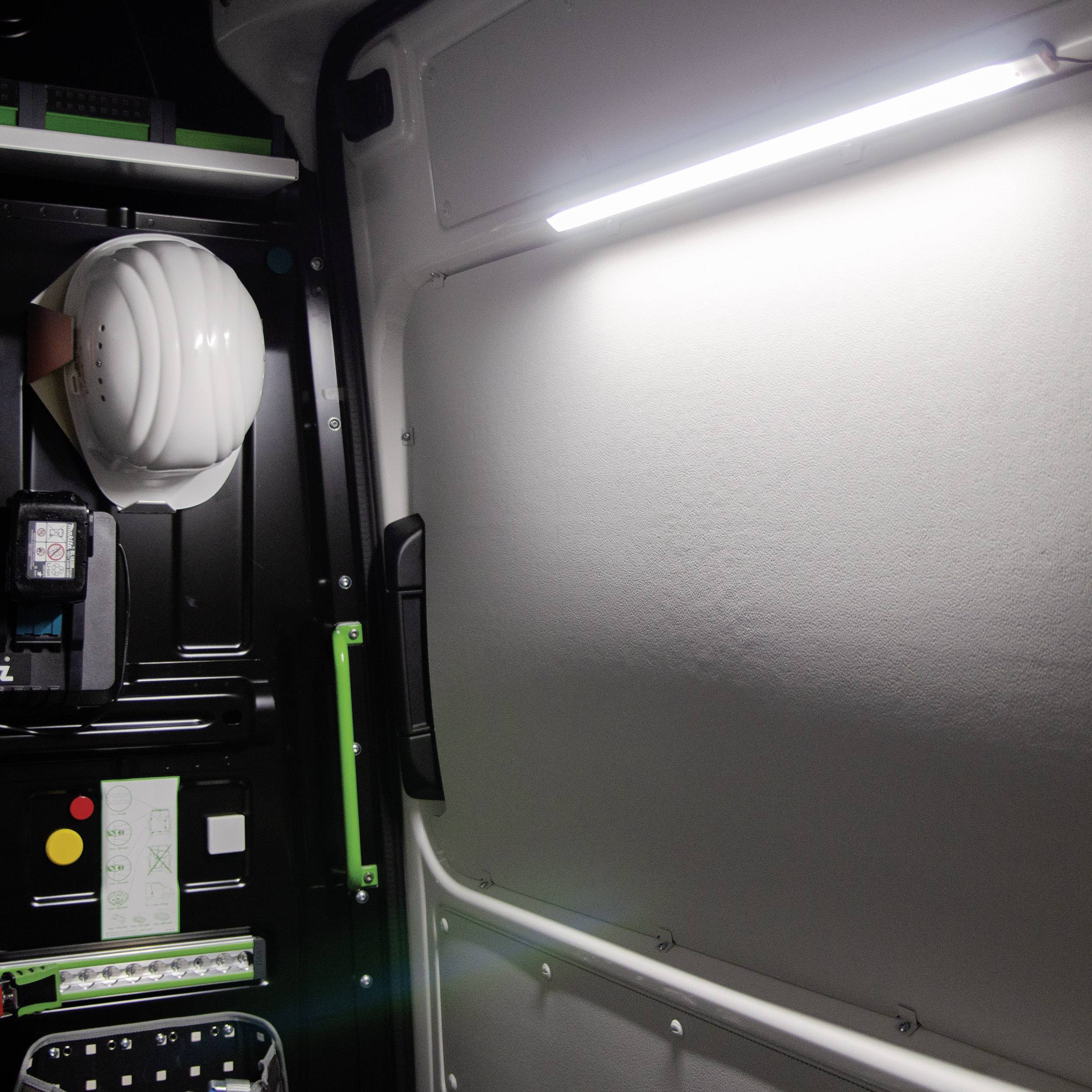 Ein Schrank mit elektronischen Geräten, Schaltern und Kabeln. Ein Schutzhelm liegt oben, Licht sorgt für Beleuchtung.